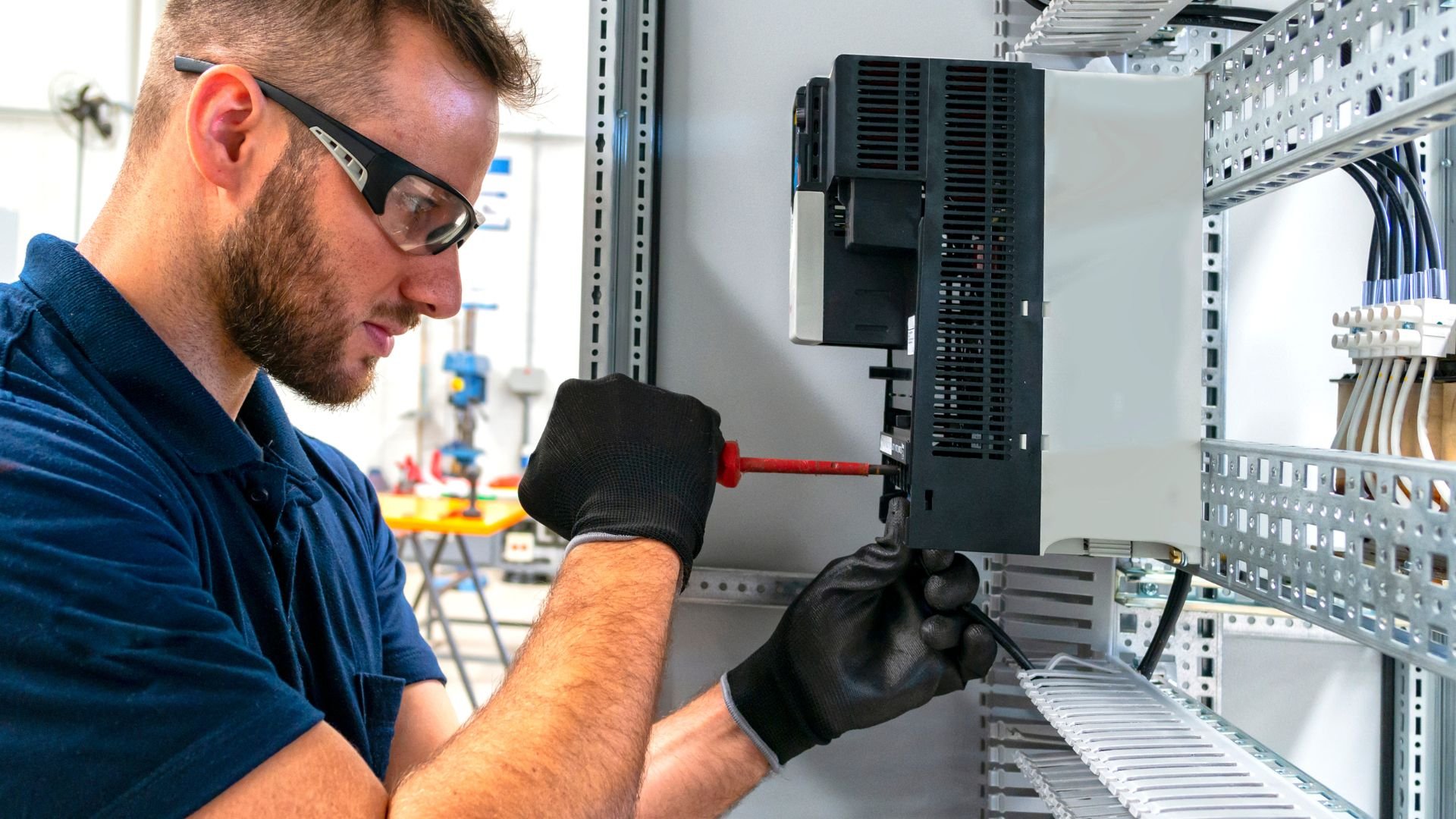 Technician in safety glasses working on electrical panel with screwdriver
