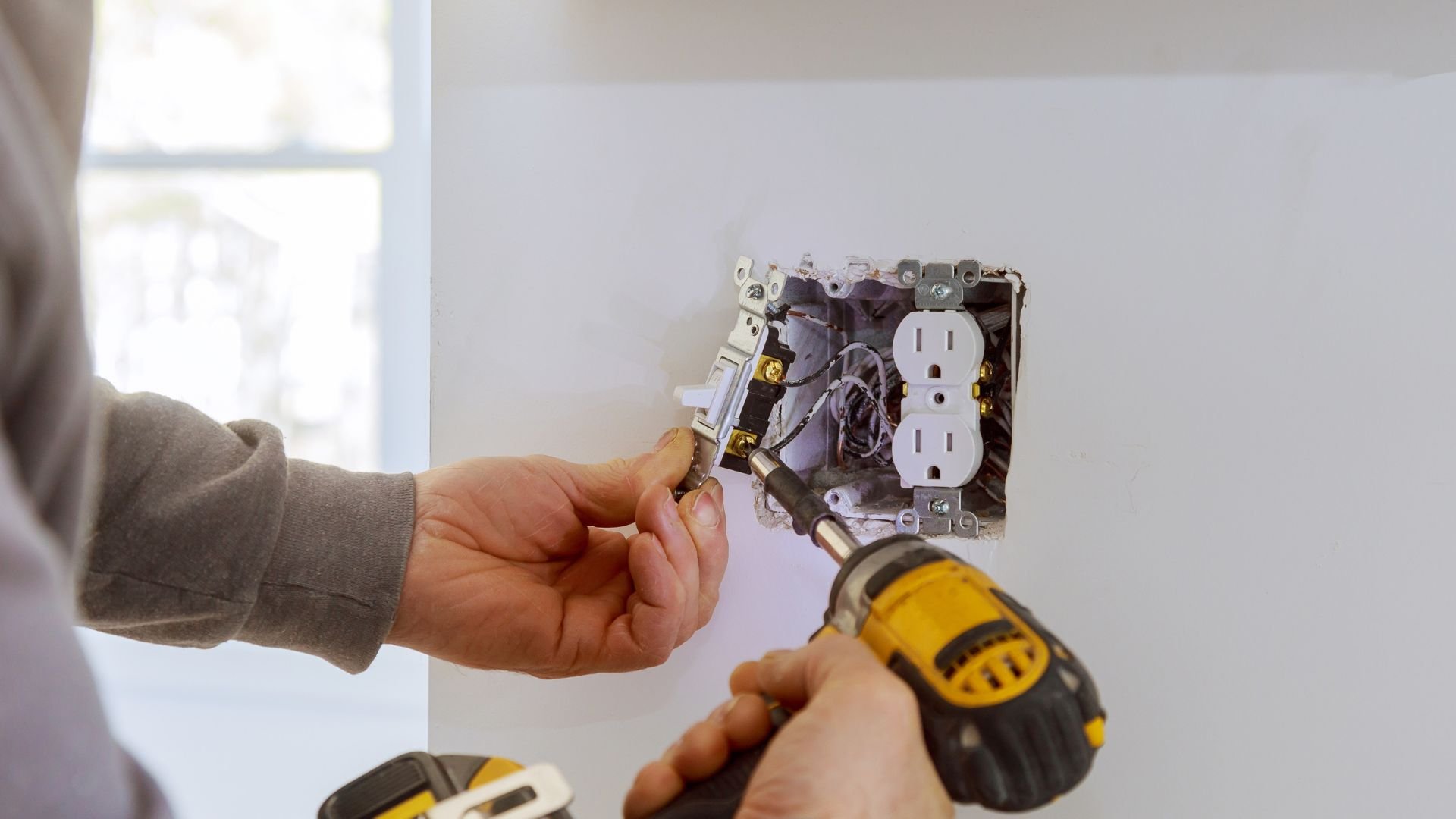 Electrician installing electrical outlet using a yellow power drill