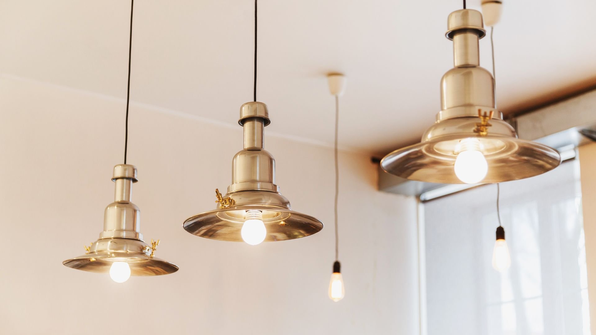 Gold metallic pendant lights hanging from ceiling with warm white bulbs