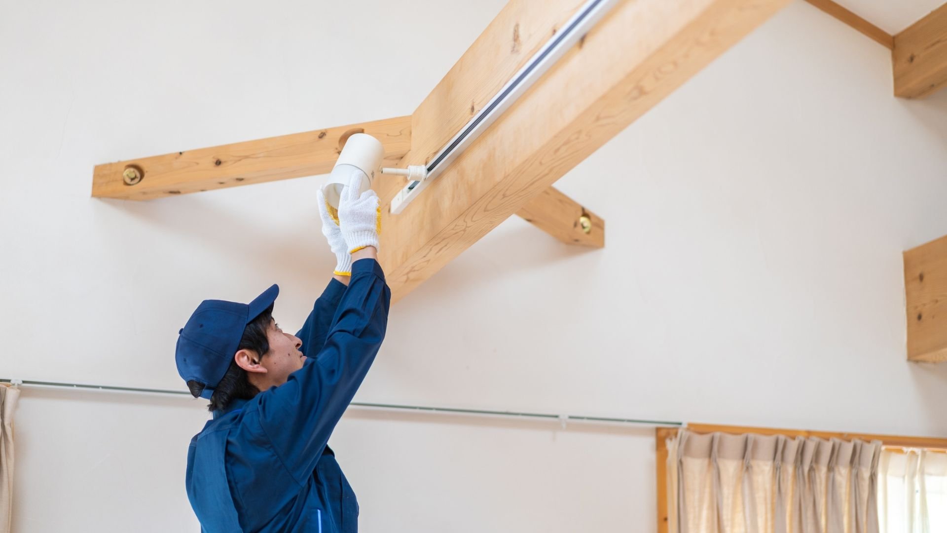 Worker in blue uniform installing or repairing ceiling pipe