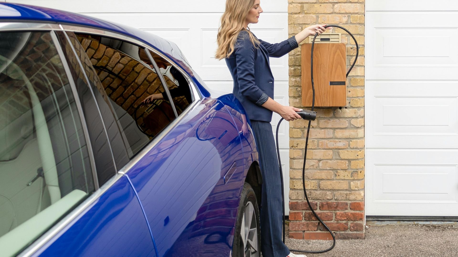 Woman charging blue electric car at home charging station