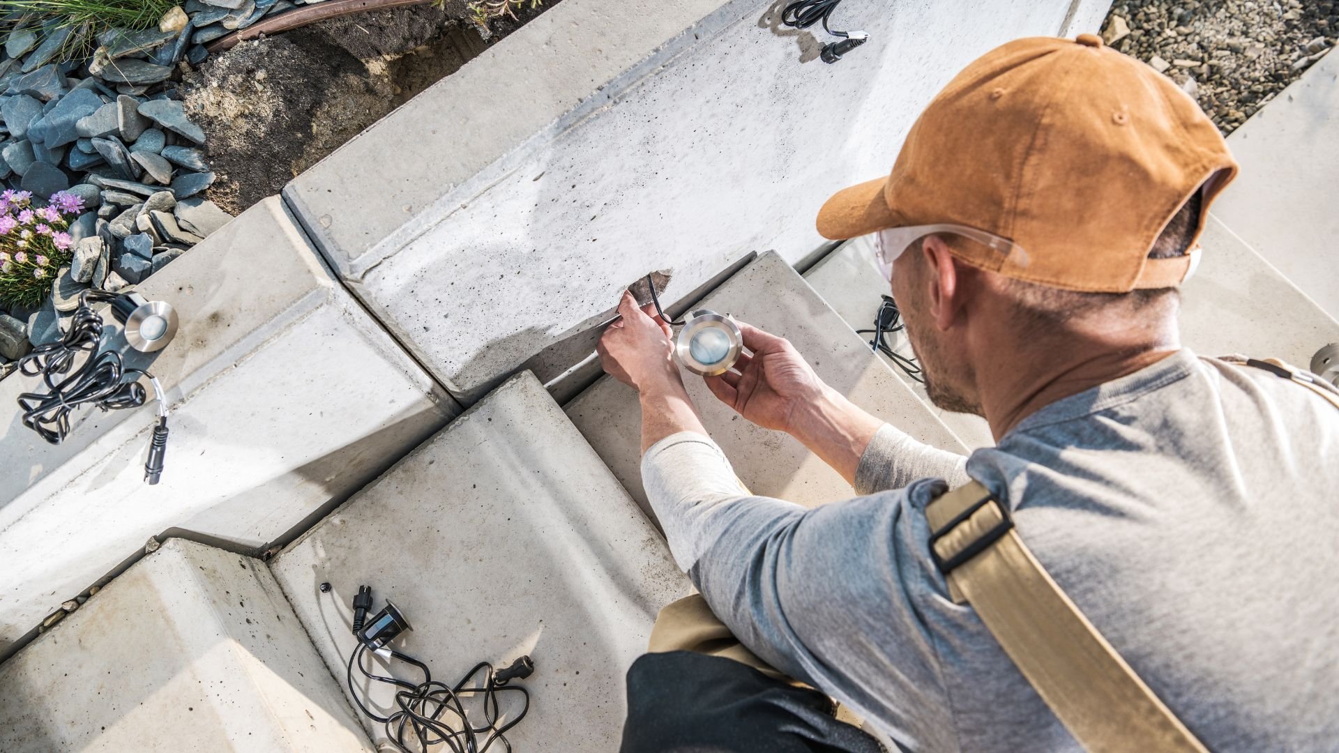 Worker installing lights on concrete steps with landscaping stones