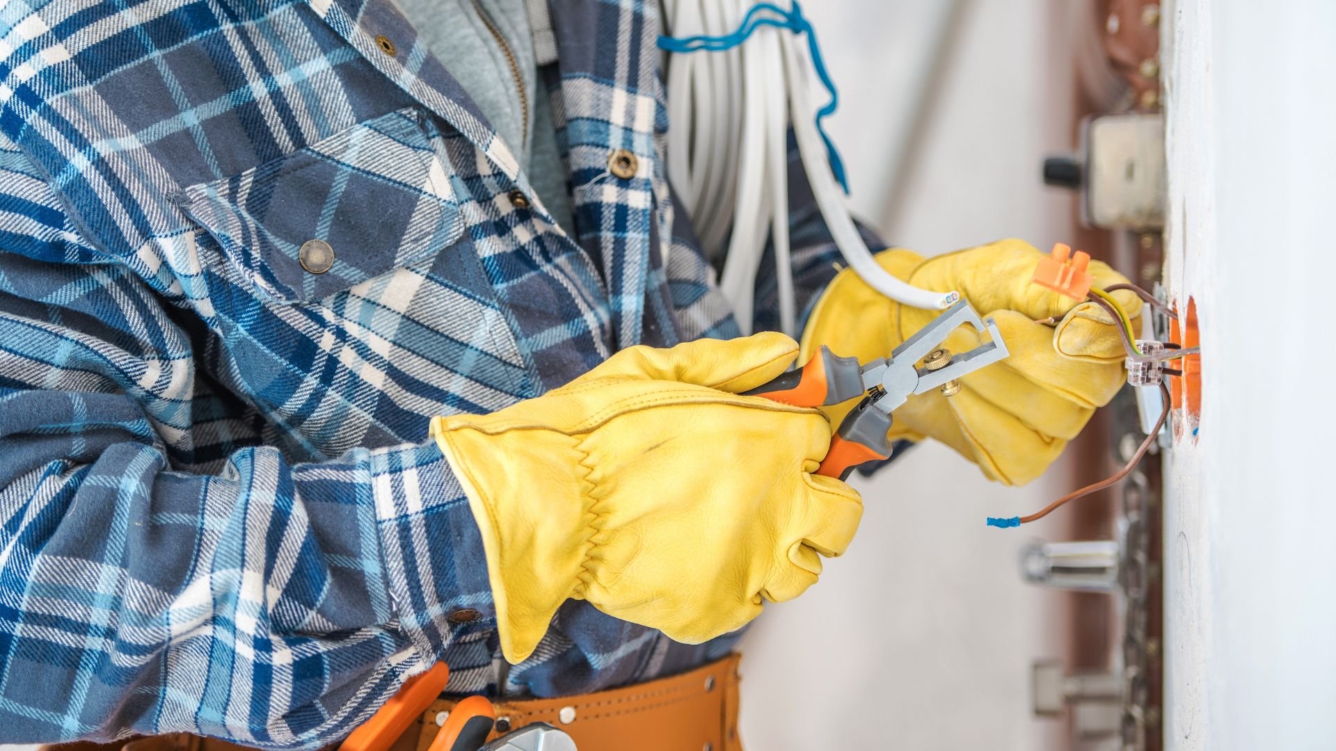 Electrician in plaid shirt and yellow gloves working on electrical wiring