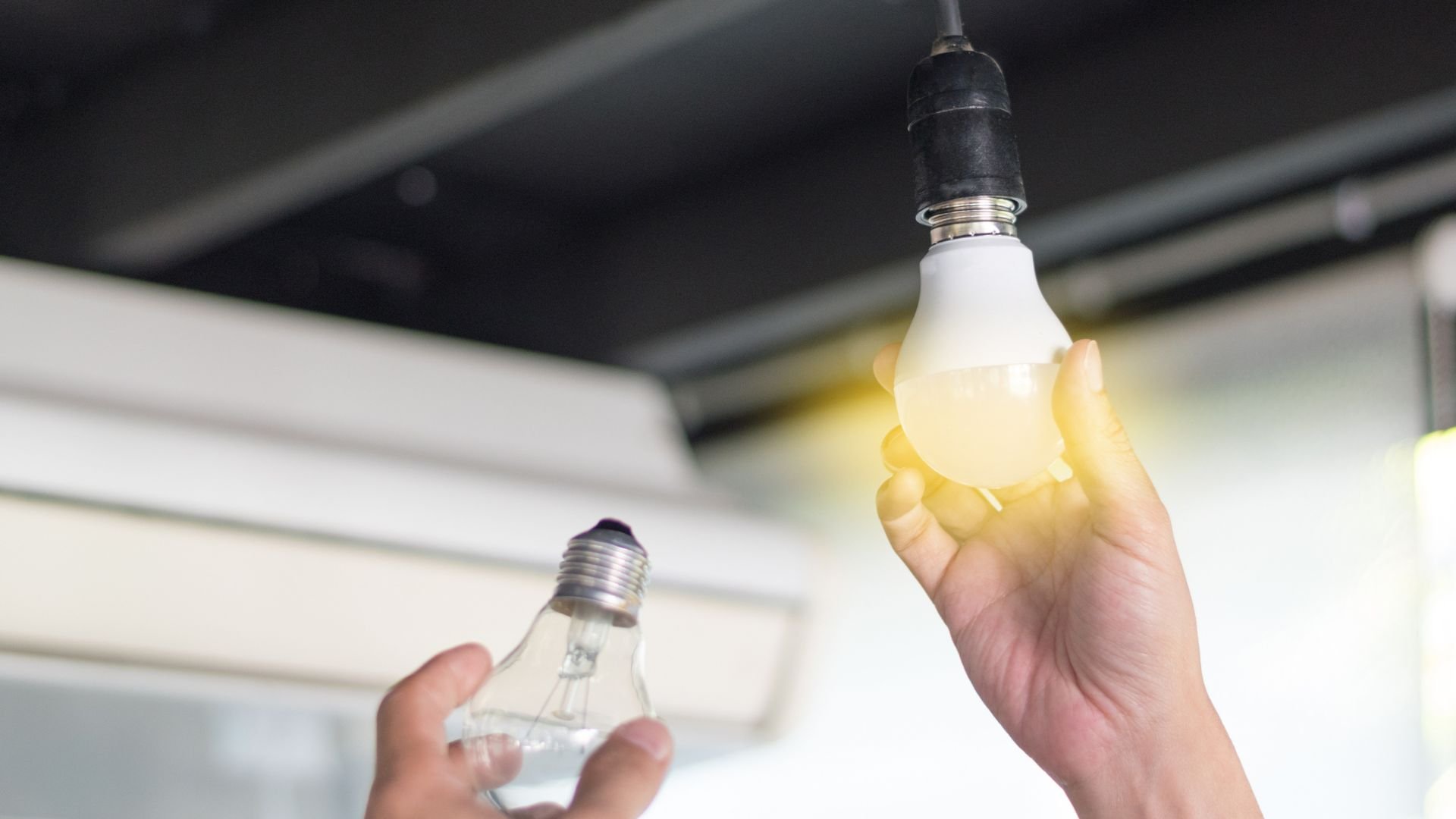 Hands changing light bulb, comparing old incandescent and new LED bulb