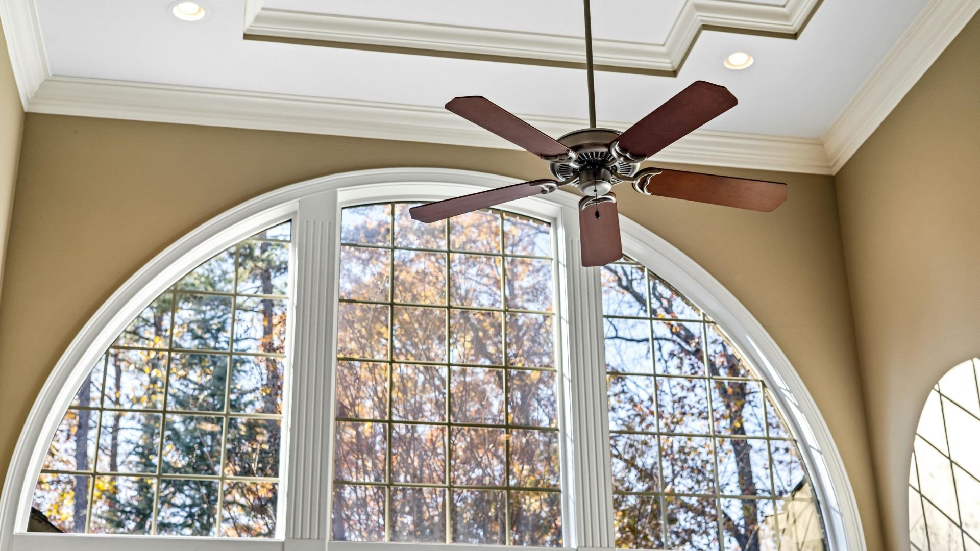 Arched window with autumn trees, ceiling fan, and warm beige walls